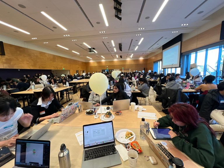 Students sitting around a table working on their laptops at the WINFO 2025 Hackathon.